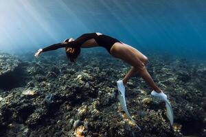 Freediver woman posing over coral reef with sun rays in tropical ocean photo