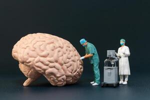 Miniature people of surgeons examining a large brain model photo
