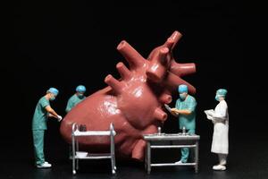 Miniature medical professionals performing a procedure on a large, anatomically accurate heart model. photo