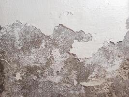 Weathered Wall Texture with Peeling Paint revealing the underlying concrete or plaster. The surface is uneven and shows signs of wear and tear, with cracks, chips, and exposed patches photo