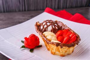 Chocolate Waffle Boat with Fruit and Ice Cream filled with fresh strawberries, sliced bananas, and a scoop of creamy vanilla ice cream in plate isolated on table side view of indulgent dessert photo