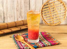 Spring Bud Grapefruit iced tea or Vibrant Layered Fruit Tea filled with ice cubes served in tall glass isolated on napkin side view on wooden table of taiwan drink photo