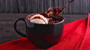 Indulgent Chocolate Lava Cake in a Mug with scoop of vanilla ice cream, drizzled with chocolate sauce isolated on napkin on a dark gray background side view of indulgent dessert photo