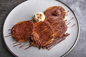 Chocolate Nutella Pancake Stack drizzled with rich chocolate sauce and topped with chocolate candy balls and vanilla ice cream served on a white plate in the background top view of dessert photo