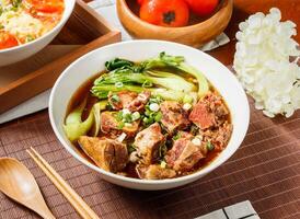 Beef Noodle Soup with Tender Braised Beef in bowl isolated on table side view of taiwan food photo