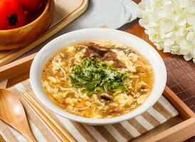 Hot and Sour Soup with Egg and Vegetables in bowl served on wooden tray napkin side view on table taiwan food photo