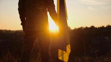 Male ukrainian army soldier stands with national banner against background of beautiful sunset. Young man in camouflage uniform with Ukraine flag as symbol of victory against russian aggression photo