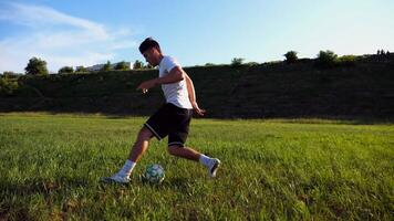Professional footballer in uniform shows tricks with ball while running at green field. Sportsman kicks ball during jogging at meadow on sunny day. Young man training at stadium. Freestyle football photo