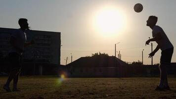 Silhouette of professional footballers kicking soccer ball with their heads on stadium at sunset. Two sportsmen showing tricks with ball while passing it to each other at field. Freestyle football photo