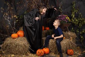 Happy mother and son playing during Halloween. cheerful family in carnival costumes in a room painted with pumpkins for the holiday of Halloween. Cheerful children playing with pumpkins and sweets. photo
