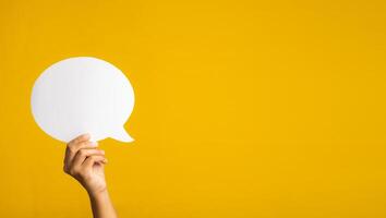 Concept of a speech bubble. Hand holding an empty speech bubble on yellow background with copy space for text. Close-up photo