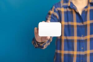 Midsection of a businessman holding a white business name card while standing with a blue background in the studio. Space for text. Business concept photo