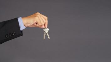 A businessman's hand holds a bunch of two keys over gray background with blank copy space for text message or information content photo