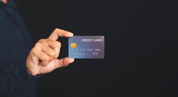 Hand of holding a mockup blue credit card while standing with a black background in the studio. Close-up photo. Money and business concept photo