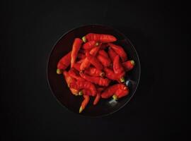 A bowl of red peppers on a black background. Top view photo