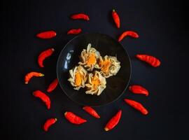 Chinese dumplings in a black bowl with red peppers photo