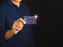 Midsection of a businessman in a blue shirt holding a mockup blue credit card while standing with a black background in the studio. Close-up photo. Space for text. Money and business concept photo