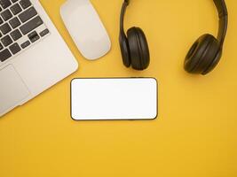 Top view of a laptop, mouse, headphones, and a smartphone isolated on a yellow background with copy space for text. Flat lay. Working desk table and relaxation concept photo