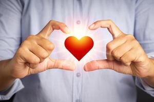 Close-up of fingers making heart figure love symbol while standing in the studio. Image red heart with light effect. Positive human emotion, feeling, body language, attitude. Valentine's day photo