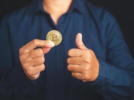 Investor hand holding a bitcoin coin and show thumbs up while standing with a black background. Bitcoin is a symbol of cryptocurrency, electronic virtual money. blockchain technology and asset digital photo