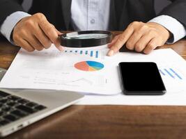 Businessman hand of holding a magnifying glass reading financial data report while sitting in the office. photo
