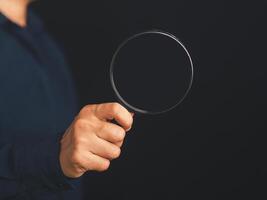 Businessman holding a magnifying glass while standing on a black background with copy space for text. Search engine optimization. Business and technology concept photo