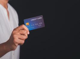 Midsection of a businessman in a white shirt holding a mockup blue credit card while standing with a black background in the studio. Close-up photo. Space for text. Money and business concept photo