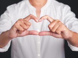 Woman in white shirt making heart figure love sign with fingers while standing in the studio. Positive human emotions, feelings, body language, attitude. Valentine's day photo