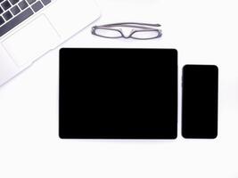 Top view of a blank tablet, smartphone, laptop, and glasses isolated on white background. Space for text. Technology and communication concept photo