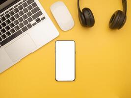 Top view of a laptop, mouse, headphones, and a smartphone isolated on a yellow background with copy space for text. Flat lay. Working desk table and relaxation concept photo