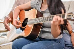 A cropped image of a boyfriend is teaching his girlfriend to play the guitar at home. photo