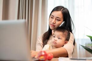 A busy mom is talking on the phone, focusing on her laptop, and taking care of her little son. photo