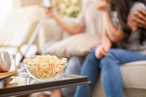 A popcorn bowl on a coffee table in the living room with a lovely couple sitting on a sofa. photo