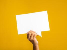 Speech bubble concept. Hand holding an empty speech balloon on yellow background with copy space for text. Close-up photo