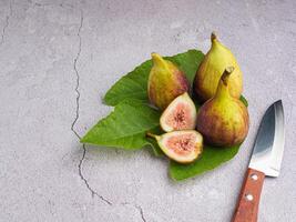 Top view of figs fruit with fresh leaves and a knife on a cement floor. High Vitamins fruit. Close-up photo. Space for text. Concept of healthy fruits and healthcare photo