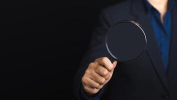Businessman holding a magnifying glass while standing on a black background with copy space for text. Search engine optimization. Business and technology concept photo