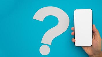 Question and communication concept. Question mark isolated on a blue background and hand holding a smartphone photo