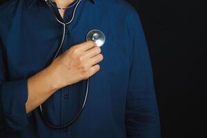 Hand of a doctor holding a stethoscope to checking heart self while standing in the studio with a black background. Space for text. Close-p photo