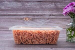 A box of sweet and sour crispy noodles or Mee krob in the Thai language with a vase of purple flowers placed on a wooden background. Side view with copy space for text photo