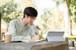 A positive and smart Asian man is working remotely at a cafe, studying online, or doing homework. photo