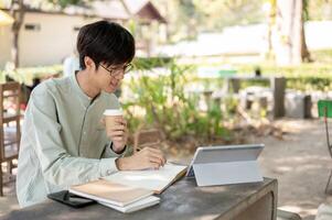 A positive and smart Asian man is working remotely at a cafe, studying online, or doing homework. photo