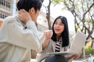 Two smart Asian students are collaborating on a project while sitting together in the park. photo