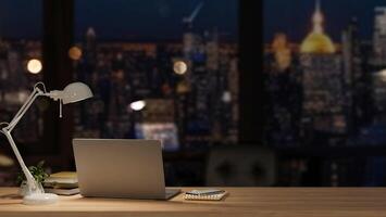 A modern office at night with a city view, featuring a laptop and accessories on a wooden desk. photo