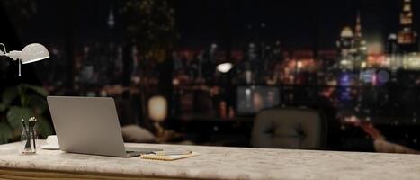 A modern office at night with a city view, featuring a laptop and accessories on a desk. photo