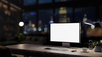 A computer desk in a modern dark office at night with a city view through the large glass window. photo