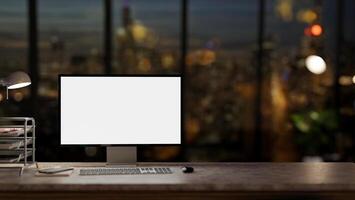 A computer desk in a modern dark office at night with a city view through the large glass window. photo