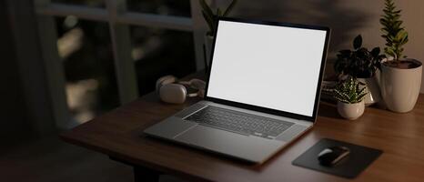 A laptop computer with a white screen mockup on a wooden table in a room at nighttime. photo