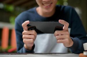A cropped image of a joyful young Asian man happily playing a mobile game on his smartphone. photo