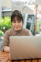 A positive Asian woman working remotely at a cafe in the city, using her laptop. photo