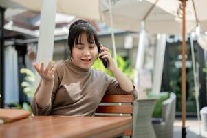 A positive woman is talking on the phone with someone while sitting at an outdoor table of a cafe. photo